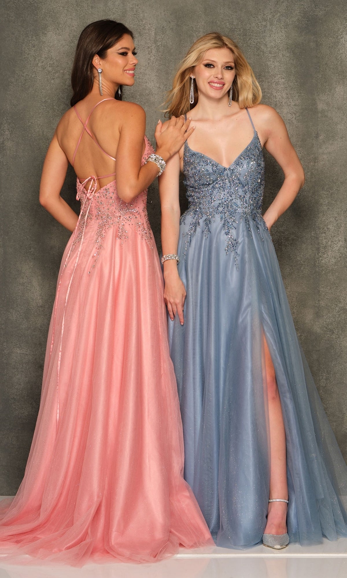Two women pose side by side in Long Formal Dress A10642 by Dave and Johnny—one wears pink with an open back, the other light blue with a v-neckline and front slit—standing against a gray backdrop.